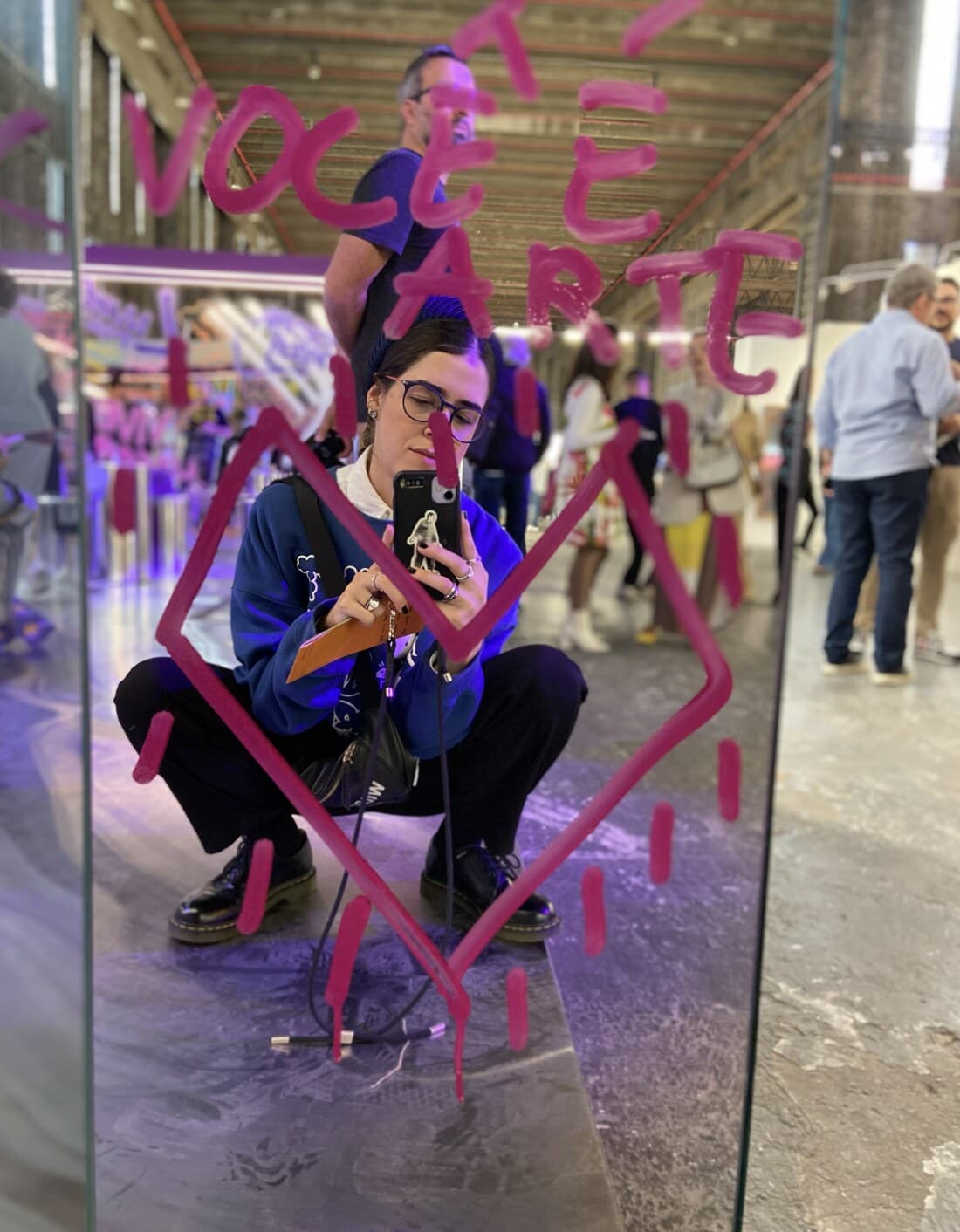 Giorgia fotografando seu reflexo em um espelho com um coração pintado em spray rosa e a frase 'você é arte'